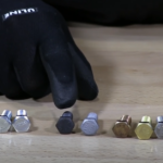 Various bolts on a table with a gloved hand pointing at one bolt