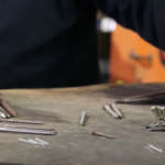 Person seated in front of a table with lots nails and hardware