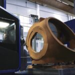 A precision engineering machine with a large brown metallic part secured on the table, within an enclosed blue cabin